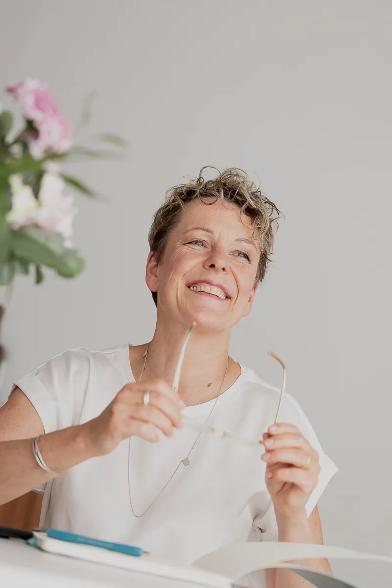 Britta Wein hält ihre Brille in den Händen und schaut entspannt.